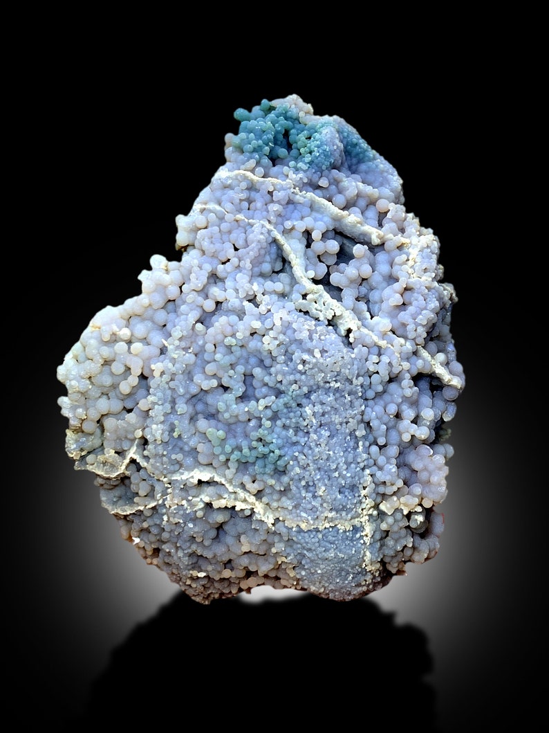 May include: A blue and white agate geode with a botryoidal texture. The geode is covered in small, round nodules that are clustered together. The geode is a natural formation and has a unique and beautiful appearance.