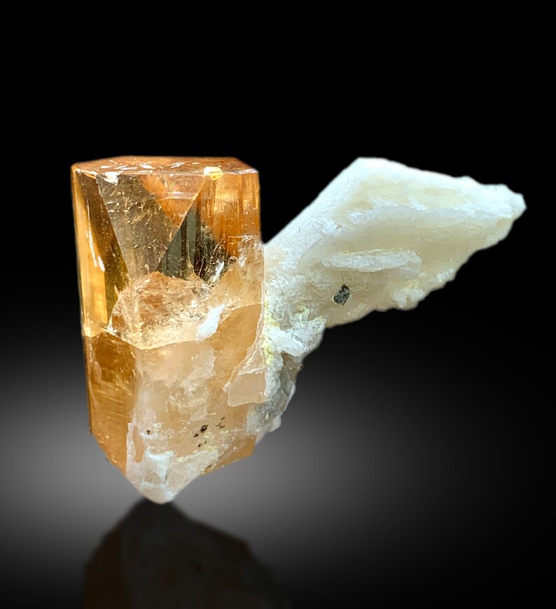 May include: A clear, orange-brown topaz crystal with a white, crystalline matrix. The crystal is sharp and well-formed, with a glassy luster.