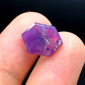 May include: A purple gemstone with a hexagonal shape and a faceted cut. The gemstone has a natural, rough texture and a deep purple color.