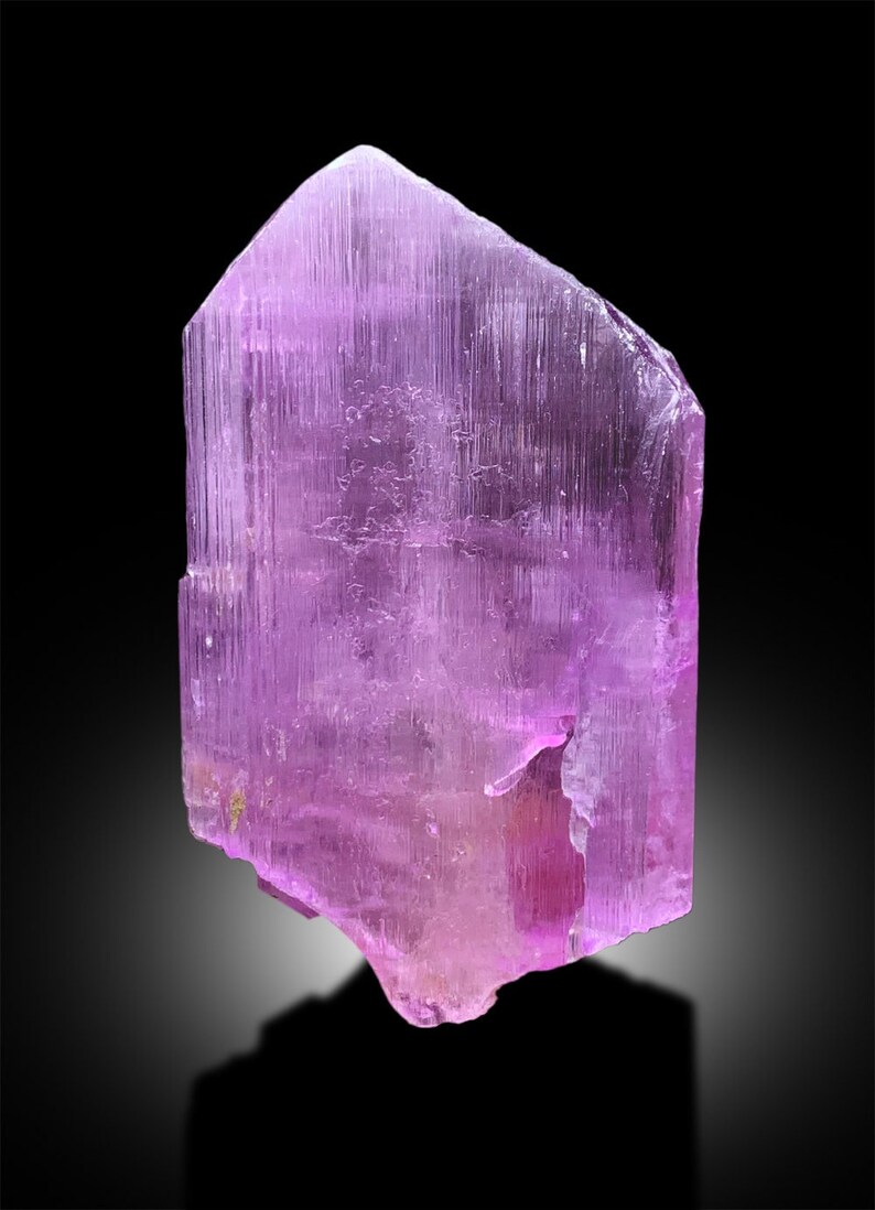 Puede incluir: Un gran cristal p&uacute;rpura transl&uacute;cido con estr&iacute;as. El cristal es facetado y tiene una punta afilada en la parte superior.