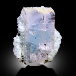 Puede incluir: Un cristal de aguamarina transparente, azul claro con un ligero tono rosado. El cristal est&aacute; en una matriz blanca rugosa.