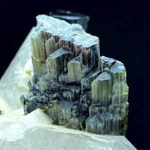 May include: A cluster of green and black tourmaline crystals on a clear quartz matrix. The crystals are sharp and well-defined, with a striated surface.