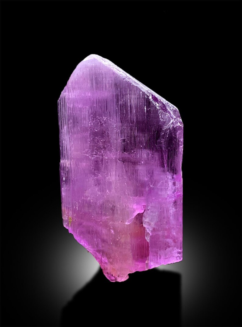 Puede incluir: Un gran cristal p&uacute;rpura transl&uacute;cido con estr&iacute;as. El cristal es facetado y tiene una punta afilada.