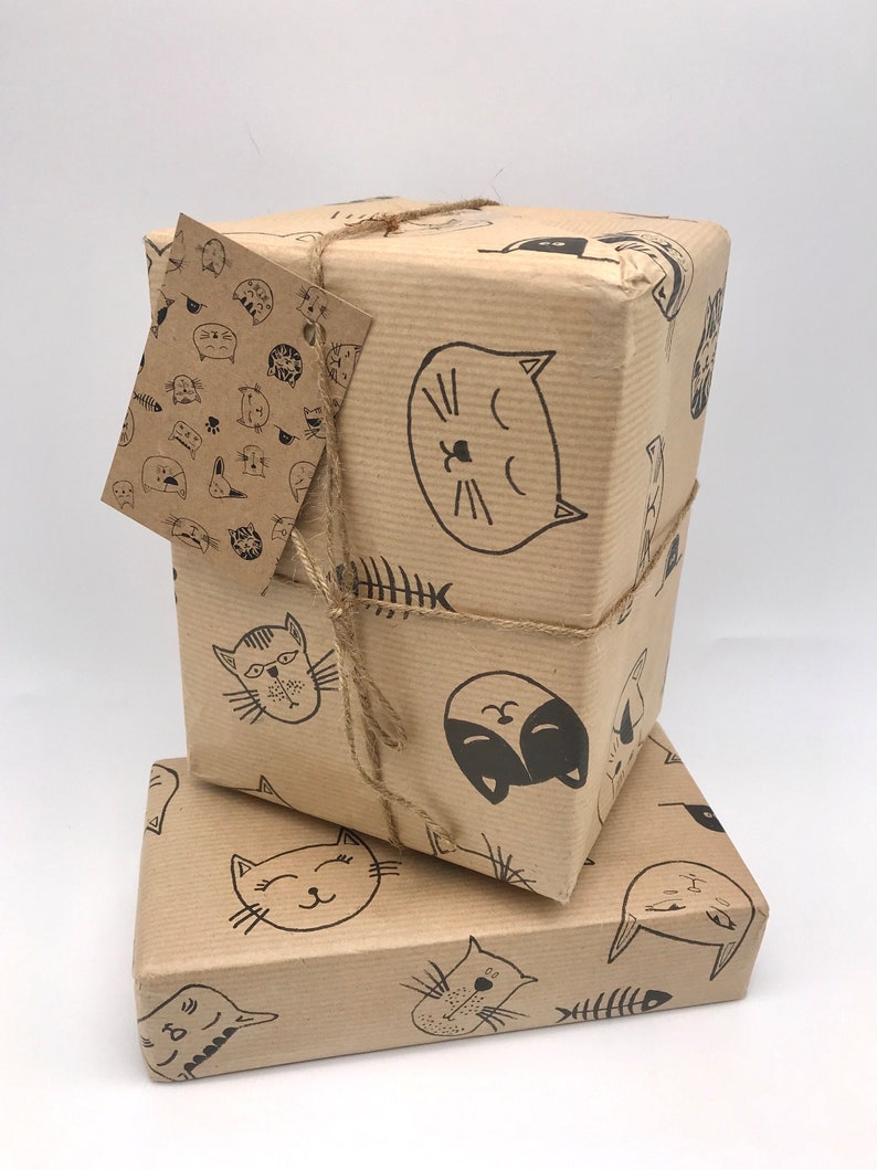 May include: Two brown gift boxes wrapped in brown paper with a black and white cat pattern. The boxes are tied with twine and have a gift tag attached to the top box.