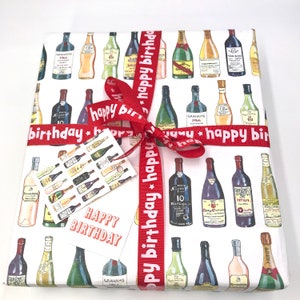 May include: Red and white gift wrap with a pattern of wine bottles. The gift wrap is tied with a red ribbon with the text "happy birthday" repeated on it. A small white gift tag with the text "Happy Birthday" is attached to the ribbon.