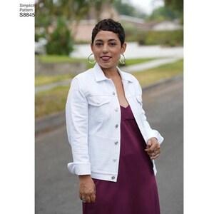 May include: A white denim jacket with a button closure and a burgundy sleeveless dress. The model is wearing silver hoop earrings.