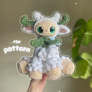 Puede incluir: Un peluche de oveja hecho a mano con ganchillo. La oveja es blanca con cara y patas beige, cuernos y bufanda verdes y ojos grandes verdes. El texto "PDF pattern" está en la imagen.