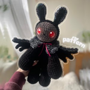 May include: A handmade black crochet bunny doll with large red eyes. The doll has long ears, a grey head, and a decorative collar. A pink ribbon is tied around the neck. The text "PDF pattern" is visible on the right side.