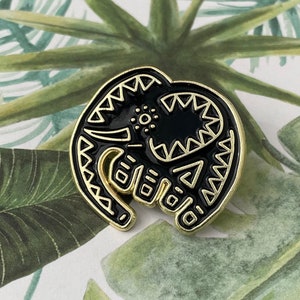 May include: Black and gold enamel pin featuring a stylized elephant design. The elephant is outlined in gold and has a black interior with gold geometric patterns.