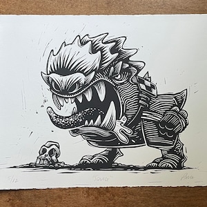 May include: Black and white linocut print of a cartoon monster with a skull in the foreground. The monster has a large mouth with sharp teeth and a long tongue. The print is titled "Saug" and is numbered 5/12.