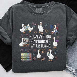 Könnte beinhalten: Dunkelgraues Sweatshirt mit einer Grafik von weißen Gänsen, die verschiedene Kommunikationsmethoden verwenden. Der Text lautet: „Wie auch immer Sie kommunizieren, ich höre zu.“ Das Design umfasst Herzen, Sterne und Blumen.