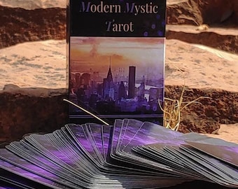 May include: A deck of Modern Mystic Tarot cards with a purple and black design, sitting on a red rock with a mountain range in the background.