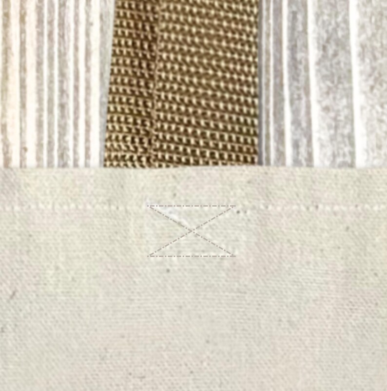 Op de afbeelding: Close-up van een canvas draagtas. De tas heeft een natuurlijke, gebroken witte stof met een versterkte handgreep en een gestikt X-detail. De handgreep is van geweven bruin materiaal en de achtergrond heeft verticale strepen.