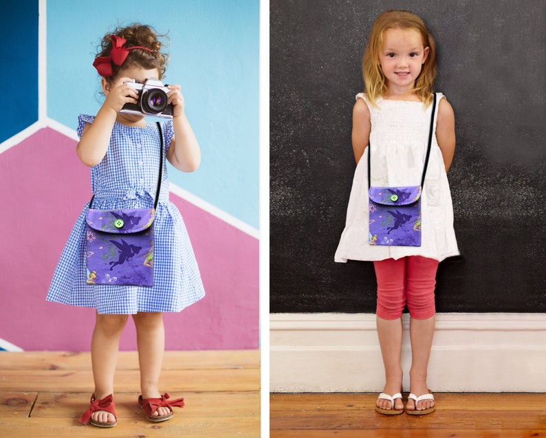 May include: Two children wearing purple and green fairy-themed crossbody bags. The bags have a flap with a button closure and a black adjustable strap.