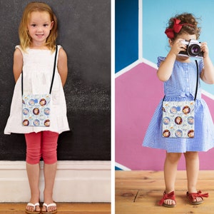 May include: Two children wearing white and blue dresses with a white crossbody bag featuring a cartoon print of two girls. The bag has a black strap. The girl on the left is wearing red pants and white sandals. The girl on the right is holding a camera and wearing red sandals.