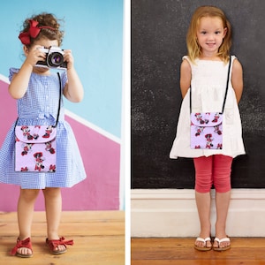 May include: Two children wearing colorful dresses and carrying small purple purses with a cartoon character print. The purses have adjustable straps and are worn crossbody.