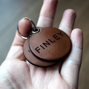 May include: Two brown leather keyrings with a silver ring. The top keyring has the name "FINLEY" engraved on it.