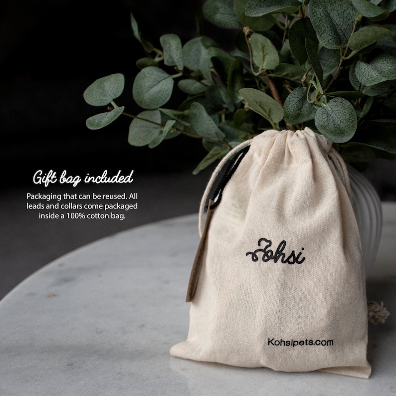 May include: A white cotton drawstring bag with black embroidery that reads "ohsi" and "Kohsipets.com". The bag is sitting on a white surface. Gift bag included. Packaging that can be reused. All leads and collars come packaged inside a 100% cotton bag.