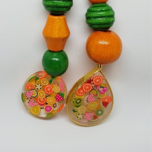 Puede incluir: Dos llaveros coloridos con temática de frutas con cuentas de madera. Un llavero tiene un dije de resina redondo lleno de rodajas de fruta de colores. El otro llavero tiene un dije de resina en forma de lágrima lleno de rodajas de fruta.