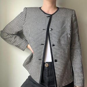 May include: Black and white houndstooth blazer with a black trim and buttons. The jacket has a classic pattern and a tailored fit. The blazer is a stylish addition to any wardrobe.