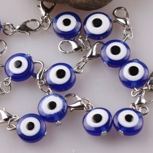 May include: Close-up of several blue and white evil eye charms with silver-colored lobster clasps. The charms have a dark blue center with a white ring and a black pupil. The clasps are attached to small silver chains.