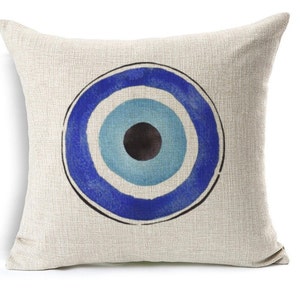 May include: Square decorative pillow with a beige linen texture. The pillow features a large, stylized eye design in shades of blue and a black center. The eye symbol is a popular motif in home decor.