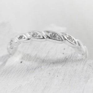 May include: A silver band ring with a twisted design and small clear stones set into the band.
