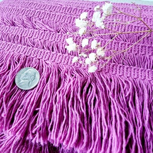May include: Purple fringe trim with a woven texture. The fringe is long and flowing, creating a soft and delicate look.