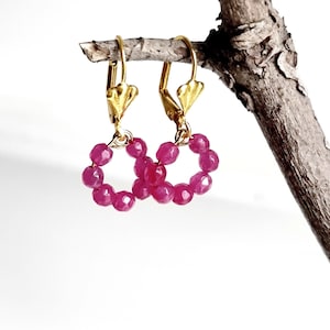 Può includere: Un paio di orecchini a cerchio dorati con perline di pietre preziose rosa. Gli orecchini sono appesi a un ramo.