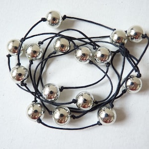 May include: A silver bead necklace with black string. The necklace has multiple strands of string and is adorned with round silver beads.