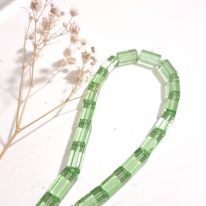 Può includere: Una collana di perline di vetro verde chiaro, ogni perlina ha la forma di un prisma rettangolare.