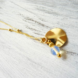 Pode incluir: Um colar de corrente de ouro com um pingente redondo de ouro martelado e uma conta de vidro azul claro.