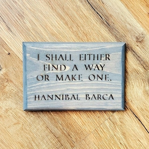 May include: A gray wooden sign with the quote "I shall either find a way or make one." attributed to Hannibal Barca.