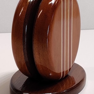 May include: A wooden desk accessory with a glossy finish. The piece is composed of two rounded, connected sections, one with vertical stripes and the other with a dark wood accent. It rests on a circular base, all in shades of brown.