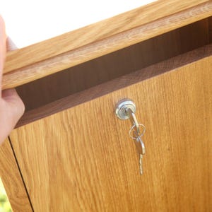 May include: A wooden box with a keyhole and a key in the lock. The box is made of light brown wood and has a natural finish.