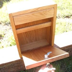 May include: A wooden box with a drawer and a hinged door. The door is open and the inside of the box is visible. The box is made of light wood and has a natural finish.