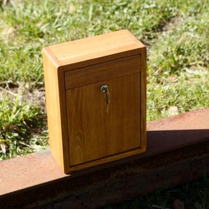 May include: A wooden box with a keyhole and a drawer. The box is made of light brown wood and has a natural wood finish.