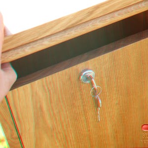May include: A wooden mailbox with a keyhole and a silver key. The mailbox is closed and has a wood grain pattern. The text "3D Brille verwenden" is visible on the bottom right corner of the image.