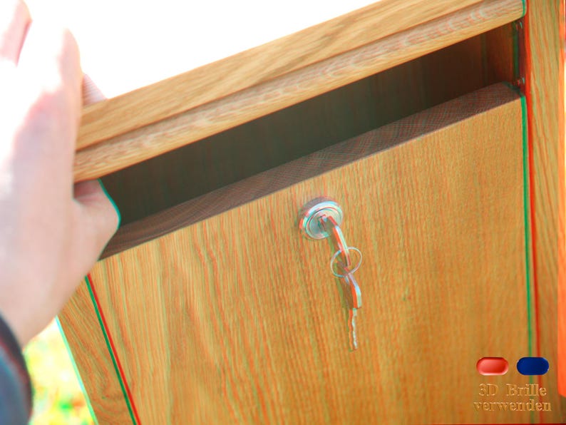 May include: A wooden mailbox with a keyhole and a silver key. The mailbox is closed and has a wood grain pattern. The text "3D Brille verwenden" is visible on the bottom right corner of the image.
