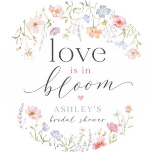 May include: A floral design with the words "love is in bloom" in black script, with the text "Ashley's bridal shower" below. The design features watercolor flowers in pink, peach, and blue hues, arranged in a circular pattern.