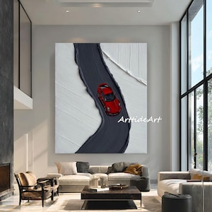 May include: Abstract painting of a red sports car on a dark grey road, set against a textured white backdrop. The artwork is displayed in a modern living room with neutral furniture and large windows, creating a contemporary feel.