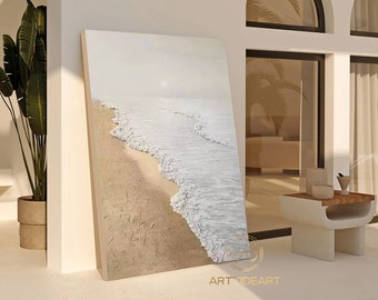 May include: A large, rectangular canvas leaning against a white wall. The artwork depicts a textured beach scene with white waves crashing on a sandy shore. The sky is a soft, pale color. The artwork is signed "ART IDEART".