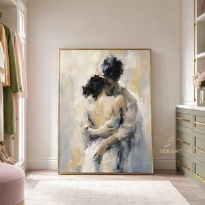 Puede incluir: Un cuadro rectangular sobre lienzo que muestra una representación impresionista de dos figuras abrazadas, en tonos suaves de azul, crema y blanco con pinceladas visibles, enmarcado en un fino marco dorado sobre una pared clara.