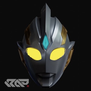 May include: A silver and gold mask with yellow eyes and a teal forehead gem. The mask has a stylized design with sharp angles and a prominent crest. The bottom left corner features a white logo with the letters "RAP".