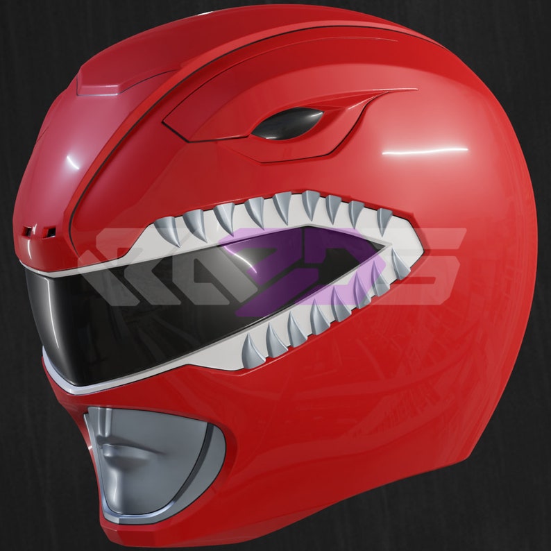 Op de afbeelding: Een rode Power Ranger helm met een glanzende afwerking. De helm heeft een gestileerde mond met witte tanden en een zwart vizier. Het ontwerp omvat scherpe hoeken en een zilveren kin, wat een futuristische uitstraling geeft.
