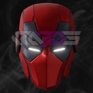 Könnte beinhalten: Ein rot-schwarzer Helm mit leuchtenden weißen Augenschlitzen. Der Helm hat ein schlankes, futuristisches Design mit kantigen Merkmalen. Das Bild hat einen dunklen Hintergrund mit einem Wasserzeichen.