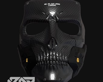 Könnte beinhalten: Eine schwarze Totenkopfmaske mit einer Kohlefaserstruktur. Die Maske hat ein detailliertes Design mit einem Skelettgesicht, einschließlich Zähnen und Augenhöhlen. Der Text "BR-10-14P-9999 LUDENS" ist oben aufgedruckt. Die Maske hat schwarze Seitenteile mit goldenen Akzenten.