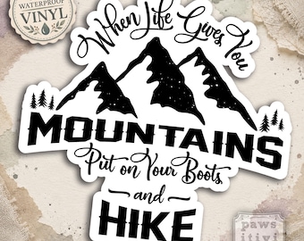Pode incluir: Um adesivo de vinil branco com um gráfico preto de picos de montanhas e pinheiros. O texto diz: When Life Gives You MOUNTAINS Put on Your Boots and HIKE. Um pequeno emblema circular indica WATERPROOF VINYL e a marca paws-itivi-tee está impressa na parte inferior.