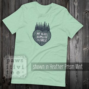 May include: A light green t-shirt with a dark blue graphic of a tree ring heart with the text "My heart belongs in the forest".
