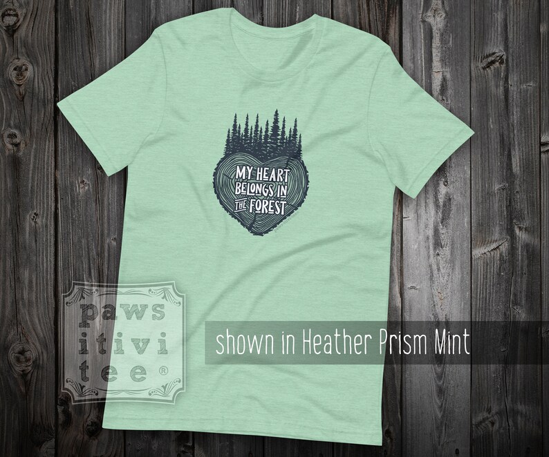 May include: A light green t-shirt with a dark blue graphic of a tree ring heart with the text "My heart belongs in the forest".